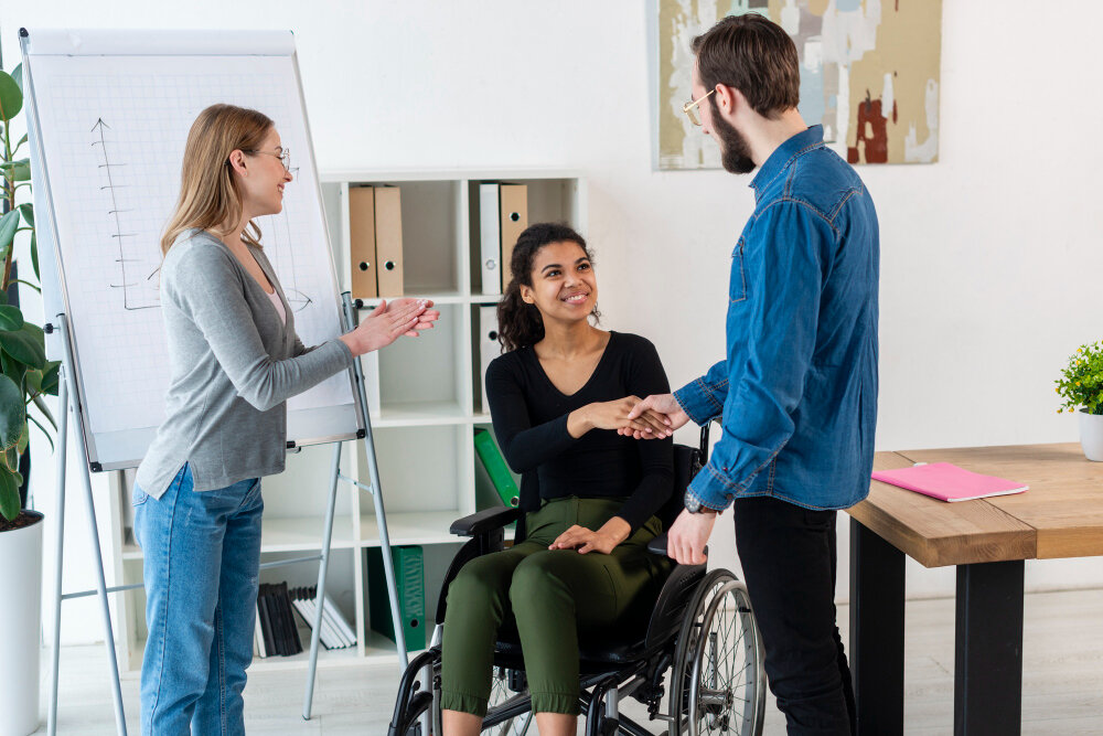 A case worker, a client using a wheelchair, and a colleague talking together in an office.
